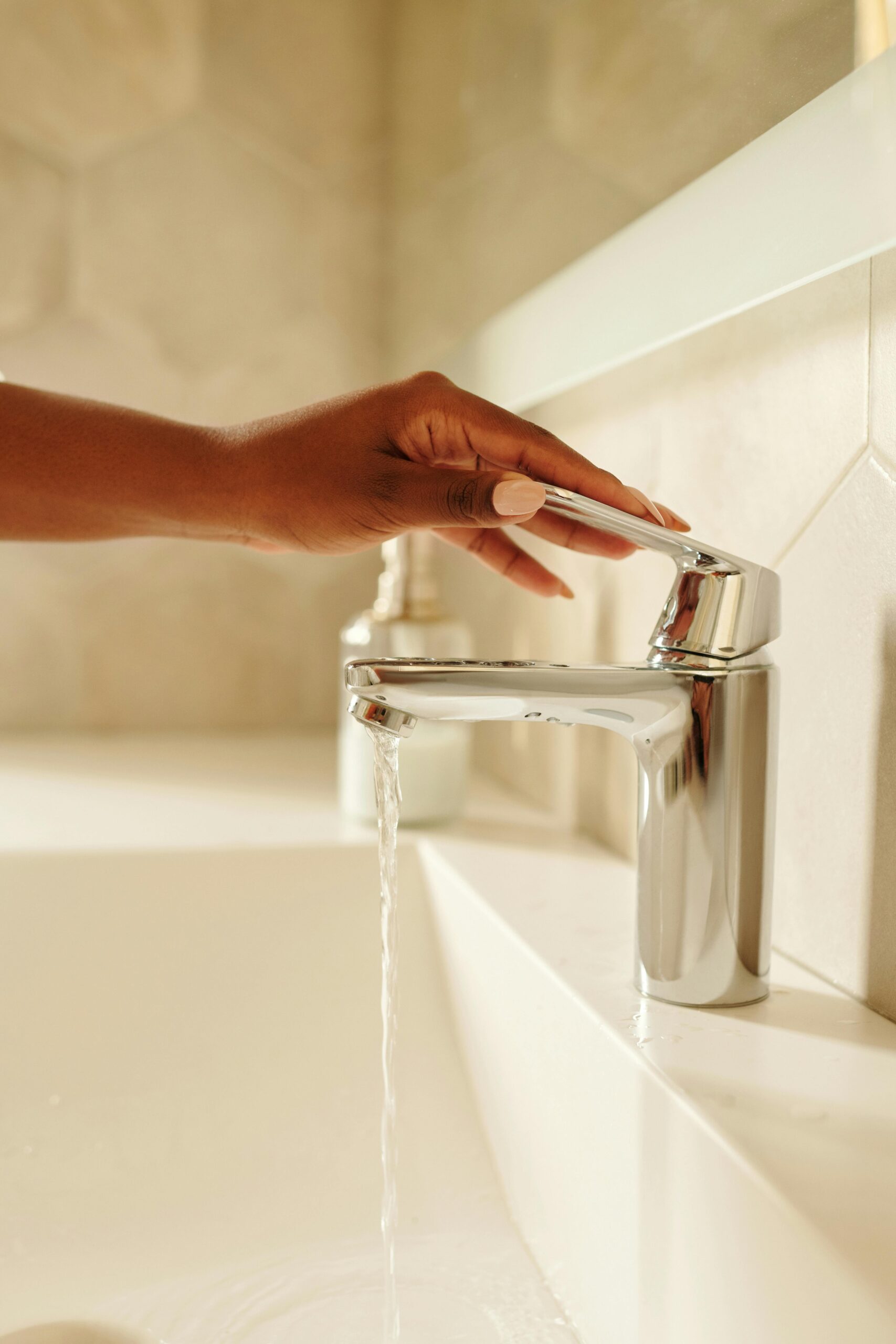 Close-up of a hand turning on a sleek chrome faucet with water flowing in a modern bathroom.