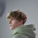 Portrait of a man with curly hair wearing a green hoodie, captured in a studio setting.